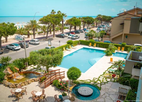 Hotel con piscina vicino al mare, circondato da palme e auto parcheggiate.